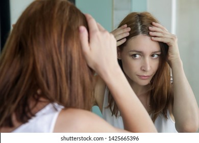 Portrait Of A Beautiful Young Woman Examining Her Scalp And Hair In Front Of The Mirror, Hair Roots, Color, Grey Hair, Hair Loss Or Dry Scalp Problem