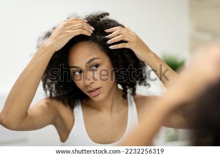 Portrait of a beautiful young woman examining her scalp and hair in front of the mirror, hair roots, color, grey hair, hair loss or dry scalp problem