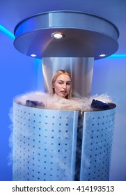 Portrait of beautiful young woman in a full body cryotherapy camber at cosmetology clinic. She is undergoing skin treatment using cold nitrogen vapors.