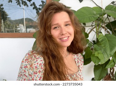 Portrait of beautiful young woman gardener in home fresh natural garden with growing green leaves, girl in summer dress is smiling and looking at camera. Eco village house or cafe  - Powered by Shutterstock