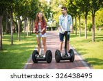Portrait of beautiful young woman and handsome man. Girl and boy using segway. Girl cheerfully smiling. Green alley as background