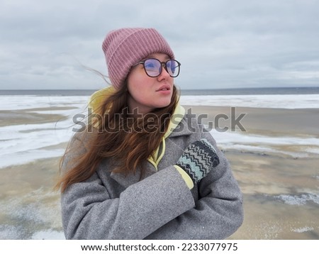 Portrait of beautiful young woman in hat, glasses and gloves  at winter cold day. Frozen girl freezing outdoors, walking