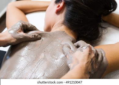 Portrait Of Beautiful Young Woman Having Clay Body Mask Apply By Beautician. Detox Ritual.