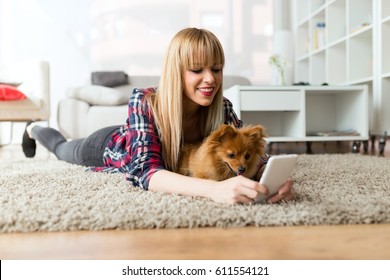 Portrait Of Beautiful Young Woman With Her Dog Using Mobile Phone At Home.