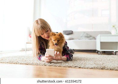 Portrait Of Beautiful Young Woman With Her Dog Using Mobile Phone At Home.