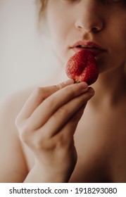 Portrait of a beautiful young woman holding a red ripe strawberry in her hand. Tenderness, white background, mood, healthy food, fruit, sexy, eat. Girl without makeup. Passion, home comfort.