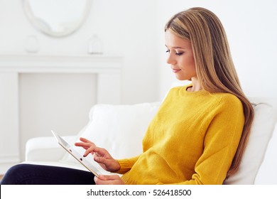 Portrait of beautiful young woman holding in her hands a digital tablet while sitting at living room - Powered by Shutterstock