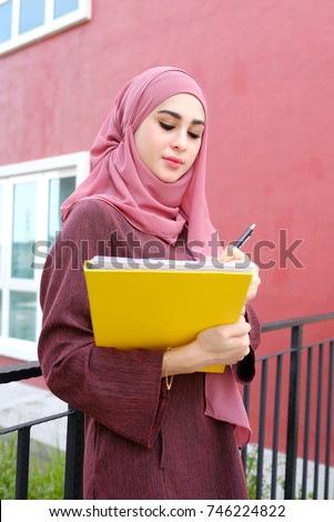 Portrait of beautiful young woman holding notebooks isolated on building background.