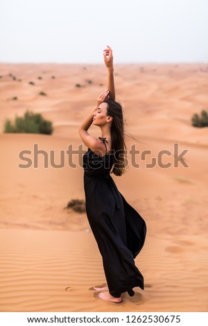 Portrait of beautiful young woman in long fluttering black dress posing outdoor at sandy desert