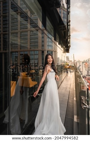 Portrait of beautiful young woman in long white dress standing on rooftop of building with cityscape scene