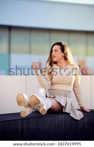 Portrait of a beautiful young woman with long wavy hair, wearing a short skirt and white blouse, posing on the terrace of a modern hotel