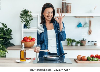 Portrait of beautiful young woman looking at camera while cooking healthy food in frying pan in the kitchen at home. - Powered by Shutterstock