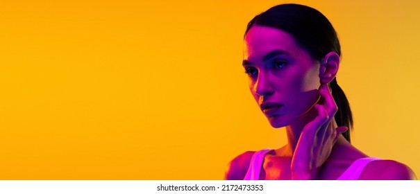 Portrait Of Beautiful Young Woman With Low Pony Tail Posing Isolated Over Yellow Studio Background In Neon Light . Concept Of Beauty, Body And Skin Care, Sport, Health, Spa, Cosmetics, Ad. Flyer