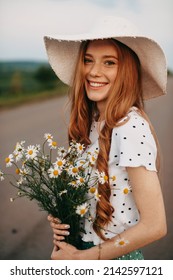 Portrait of a beautiful young woman in nature summer day with field chamomile flowers and hat. Country life. Beautiful model in warm colors. Summer