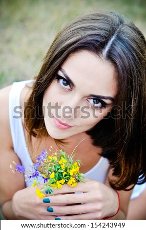 portrait of beautiful young woman in park smelling flowers