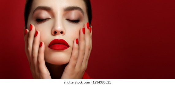 Portrait of beautiful young woman with perfect young skin, red matt lips and nails.  Model with bright scarlet color makeup and manicure posing on red background. Close up.