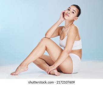 Portrait of a beautiful young woman posing in underwear while sitting in studio isolated against a blue background. Beauty shot of a confident and flawless model with soft, smooth and silky skin