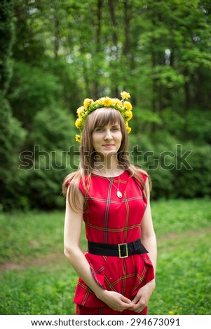 Portrait of beautiful young woman in red dress with dandelion wreath on head in forest