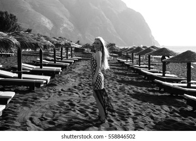 Portrait Of A Beautiful Young Woman Resting On A Black Beach On A Greek Island Santorini. Black And White Photo