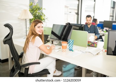 Portrait Of Beautiful Young Woman Sitting At Her Table Working On Computer And Making An Eye Contact