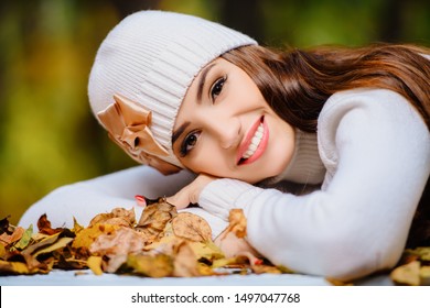 A Portrait Of A Beautiful Young Woman Sitting At A Table Covered With Golden Autumn Leaves. Lifestyle, Autumn Fashion, Beauty. 