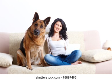 Portrait Of Beautiful Young Woman Sitting On Sofa With Her German Shepherd Dog And Netbook