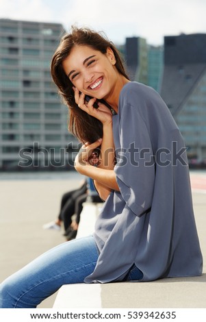 Portrait of beautiful young woman sitting outside and talking on mobile phone