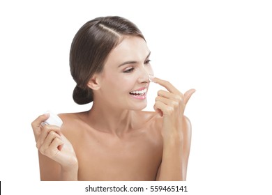 Portrait Of Beautiful Young Woman Smiling While Take Some Facial Cream And Apply To Her Nose Isolated On White Background