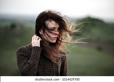 Portrait of beautiful young woman standing on the cliff, watching the last light. Hair blowing in the wind.Girl admiring mountain landscape. A woman standing alone in sunset scene - Powered by Shutterstock