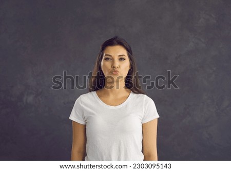 Portrait of beautiful young woman standing on gray background with folded lips in anticipation of kiss. Cheerful and flirtatious caucasian woman who is ready to take kiss. Concept of human feelings.