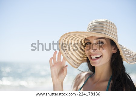 portrait of a beautiful young woman in a swimsuit on the beach protecting herself from the sun with a big hat