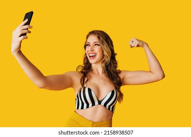 Portrait Of Beautiful Young Woman Texting Flirt Bicep Arm Muscle Selfie Photo Message With Smartphone On Yellow Background Studio