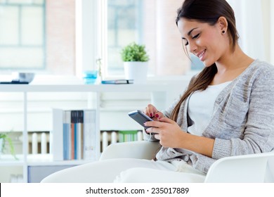 Portrait Of Beautiful Young Woman Using Her Mobile Phone At Home.