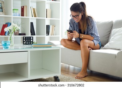 Portrait Of Beautiful Young Woman Using Her Mobile Phone At Home.