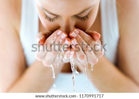Portrait of beautiful young woman washing her face splashing water in a home bathroom.