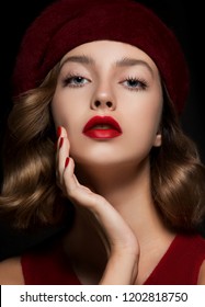 Portrait of beautiful young woman wearing red clothes and beret with perfect young skin, red matt lips and nails.  Model with bright scarlet color makeup and manicure posing on dark background.