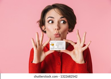 Portrait of a beautiful young woman wearing red clothes standing isolated over pink background, holding credit card - Powered by Shutterstock