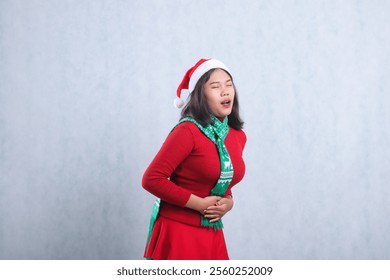 portrait of beautiful young woman wearing christmas sweater, Santa hat and scarf, left side sad close eyes both hands holding stomach ache, isolated on white background - Powered by Shutterstock