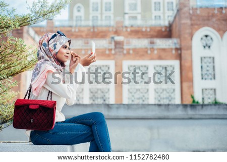 Portrait of Beautiful young woman wearing hijab applying blush on over the city background