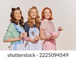 Portrait of beautiful young women, housewives with cooking tools isolated over grey background. Pop art. Concept of beauty, retro style, fashion, elegance, 60s, 70s, family. Copy space for ad