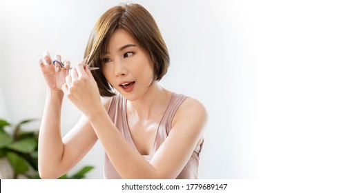 Portrait Of Beauty Asian Woman Has Scissors Hand Cutting Hair During Lockdown Of Coronavirus. Girl Have New Hairstyle Haircut, DIY Hair Cut During Covid Stay Home, New Normal Lifestyle Barber Concept