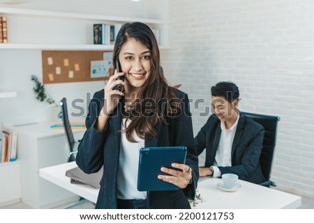 Portrait of a beauty indian business woman CEO smiling. Portrait of a positive looking young business professional standing holding tablet with co-workers talking in the background.