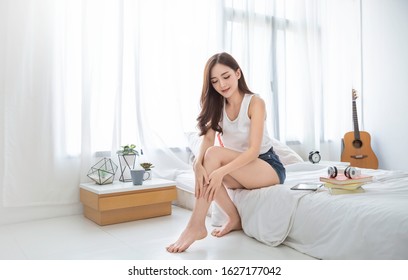 Portrait of beauty  smiling asian woman applying a lotion to her leg skin during her morning routine. Cute asian girl. Skincare body lotion, beauty clinic skincare spa indoors woman lifestyle concept