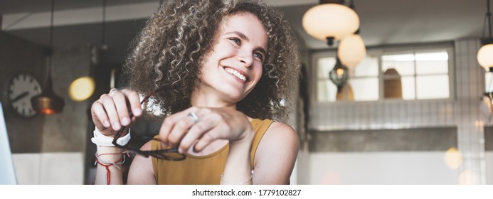 Portrait of beauty and smiling curly hair woman in city cafe, drinking coffee and holding eyeglass - Powered by Shutterstock