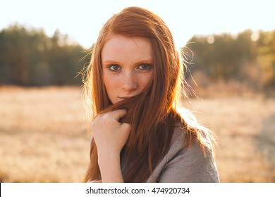 Portrait Of Beauty Teenage Model Girl With Red Hair On The Background Of Nature On The Field In Sun Light. Face Of Young Woman With Freckles. Autumn. Glow Sun, Sunshine. Backlit. Warm Color Tones