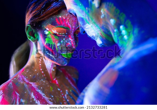 Portrait of a beefy man and\
woman painted in ultraviolet powder. Body art glowing in\
ultraviolet light