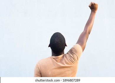 Portrait From Behind Young Black Man With Arm Raised And Fist Pump In The Air By Gray Background