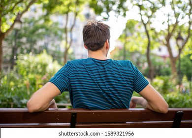 Portrait From Behind Of Young Man Sitting On Park Bench