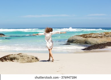 Portrait from behind of young woman walking to the water on the beach