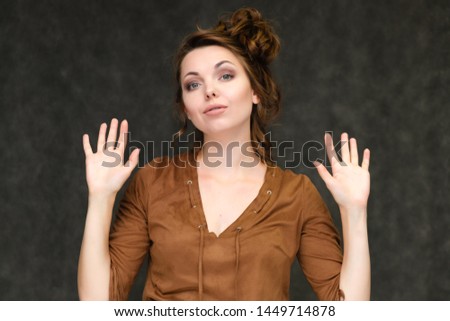 Portrait below breast over gray background of pretty young brunette woman in brown dress with beautiful hair. Standing in different poses, talking, showing with hands, demonstrating emotions.